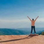 person in beige top on mountain cliff