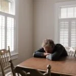 man in gray long sleeve shirt sitting on brown wooden chair
