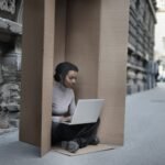 african american female sitting inside cardboard box with laptop